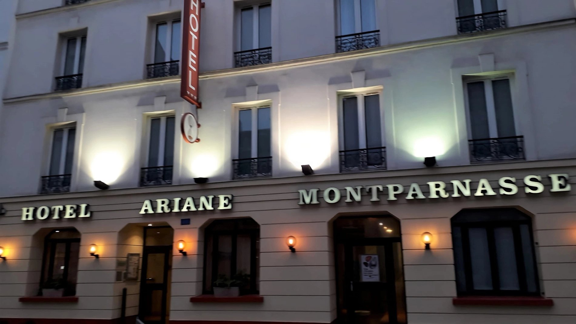 Façade de l'hôtel Ariane Montparnasse illuminée la nuit dans le 14e arrondissement de Paris, proche de la Fondation Cartier et de la Tour Montparnasse