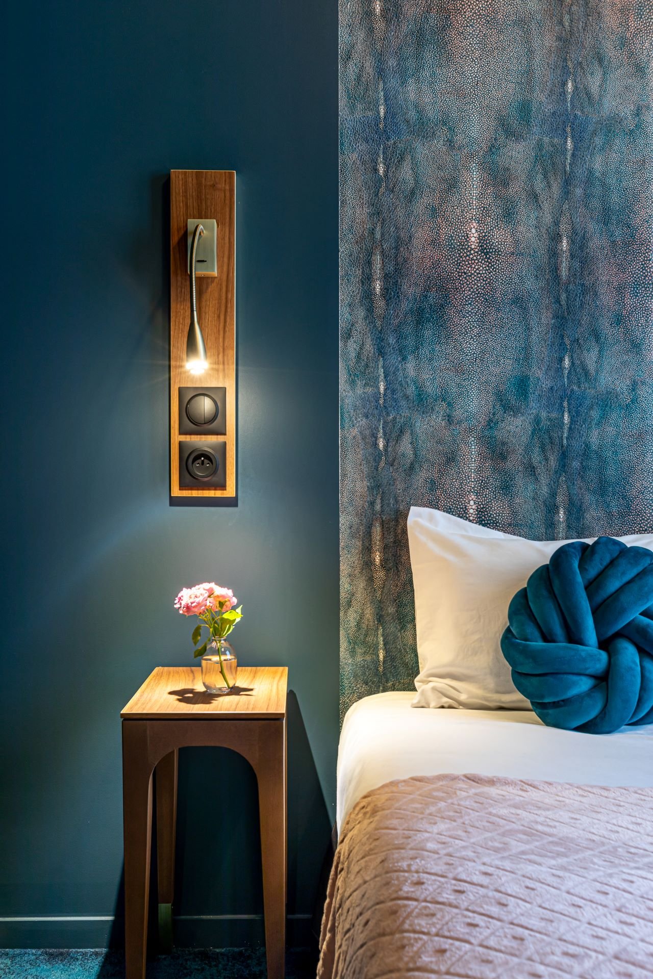 Détail de la décoration intérieure de l'Hôtel Glasgow Monceau à Paris, mettant en valeur une table de chevet en bois, un élégant coussin décoratif et une tête de lit en galuchat.