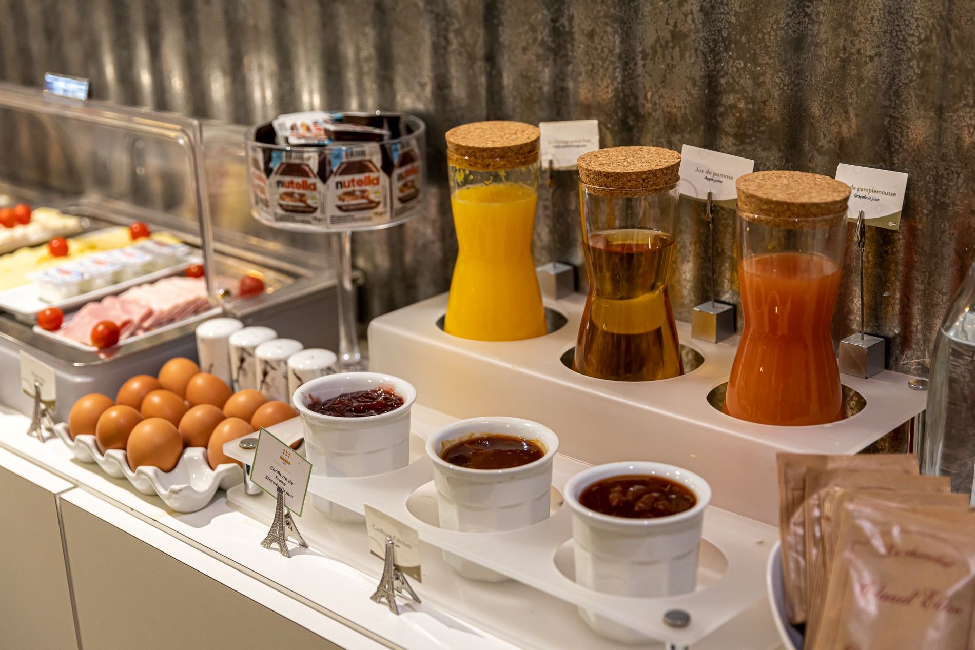 Buffet de petit-déjeuner à l'Hôtel Glasgow Monceau avec jus de fruits frais, confitures, œufs, et assortiments de charcuterie et fromage.