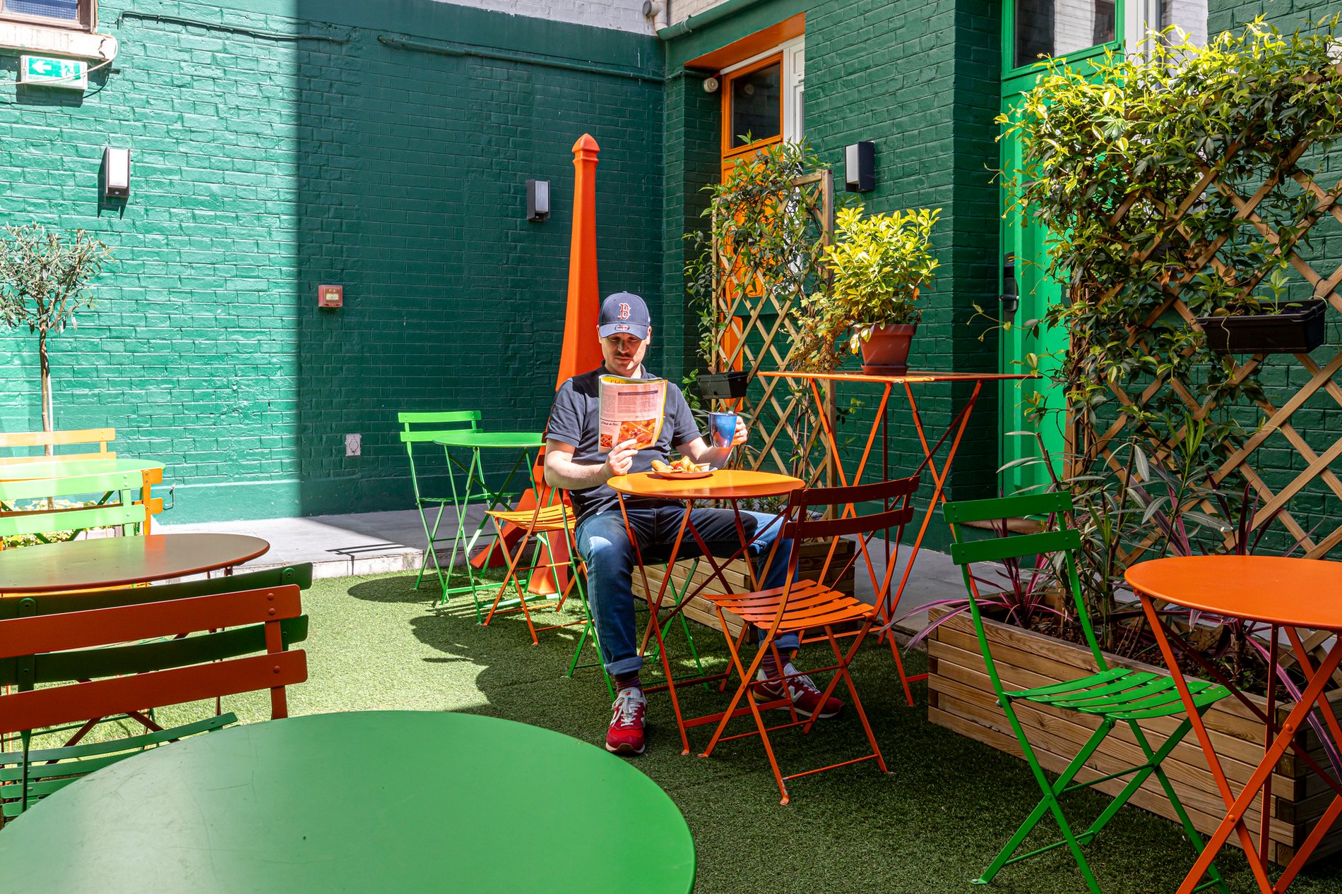 Patio extérieur de l’hôtel Alpha Paris Boulogne, terrasse colorée avec tables, chaises et plantes pour un moment de détente près de Paris.